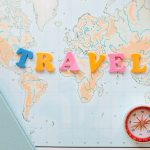 Flat lay of a map with colorful letters "TRAVEL" and a compass for planning adventures.
